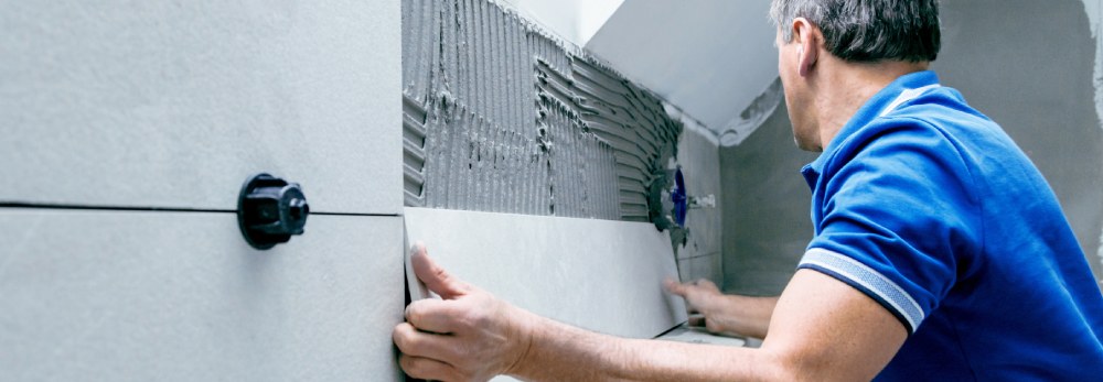 Person bringt Fliese an Wand an